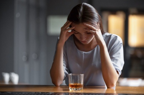 Eine junge Frau sitzt mit gesenktem Kopf vor einem alkoholischen Getränk