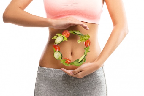 Junge Frau mit einem Kreis aus Gemüse vor dem Bauch