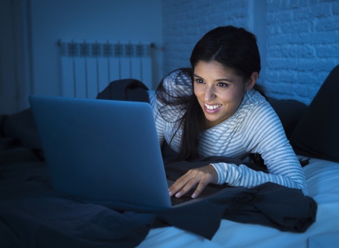 Eine Frau sitzt beim Laptop und blaues Licht erhellt den ganzen Raum