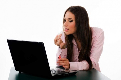 Frau im Büro die sich vor dem PC schminkt