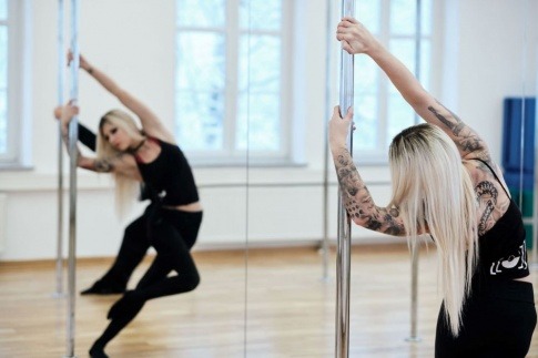 Eine blonde sportliche Frau tanzt vor einer Spiegelwand an einer Stange