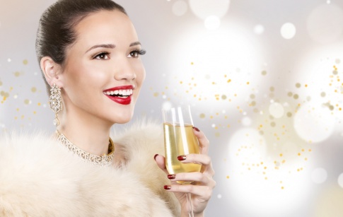 Eine Frau mit festlichem Make-up, roten Lippen und einem Champagnerglas in der Hand