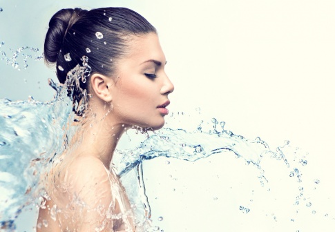 Eine Frau mit jochgesteckten Haaren im Profil. Ein Schwall Wasser bewegt sich gerade in Richtung ihr Gesicht