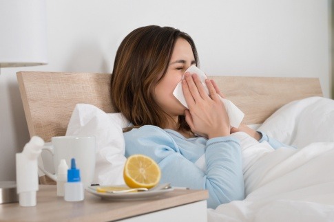 Eine Frau liegt krank im Bett mit Taschentüchern