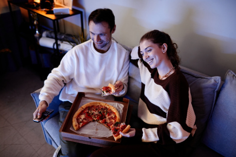 Freundschaft nach Beziehung - Mann und Frau sitzen auf Sofa, teilen sich eine Pizza und schauen TV.