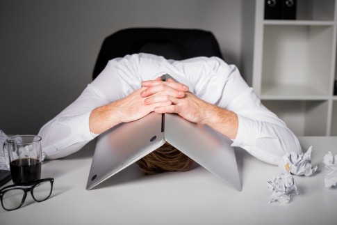 Ein frustrierter Mann versteckt sein Gesicht unter einem Laptop