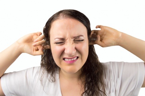 Frau hält sich die Ohren zu und wirkt sehr gestresst.