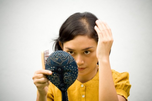 Frau untersucht Haare vor Handspiegel