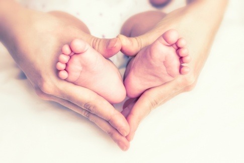 Zwei Hände eines Erwachsenen umfassen zwei Kinderfüße und formen ein Herz