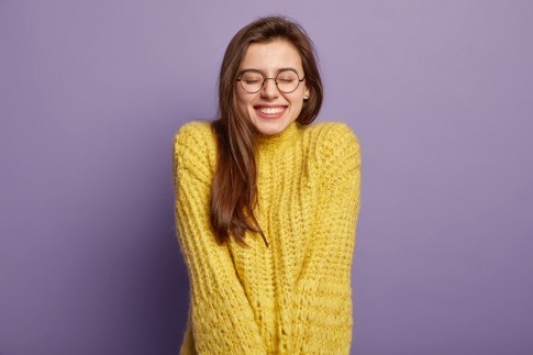 Eine junge Frau mit Brille lacht geschmeichelt und verlegen
