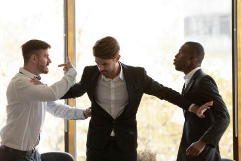 Ein Mann schlichtet zwischen zwei streitenden Arbeitskollegen