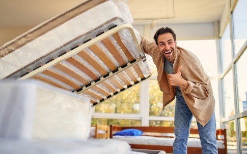 Ein Mann hebt sein Matratze hoch und zeigt lächelnd den Daumen nach oben