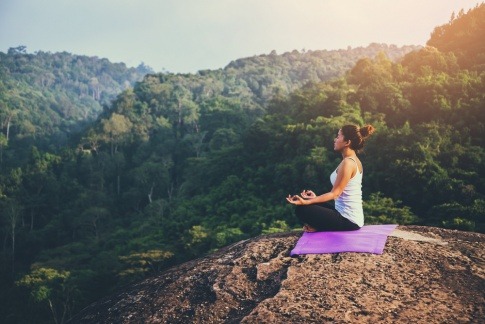 Eine Frau meditiert auf einem großen Felsen in der Natur