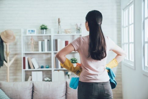 Eine Frau steht in der Wohnung mit Putzhandschuhen und Putzzeug