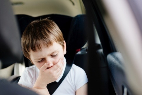 Junge hält sich bei Autofahrt die Hand vor den Mund.