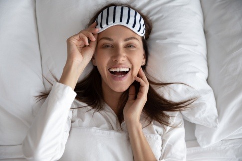 Lachende Frau mit Schlafmaske im Bett wird schön im Schlaf