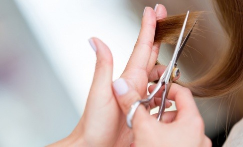 Ein Friseur schneidet die Haarspitzen einer Frau.