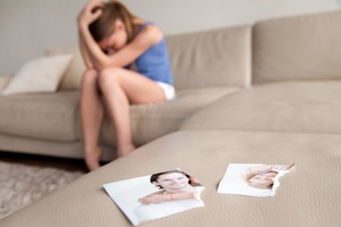 Mit der Vergangenheit abschließen - ein in zwei Teile zerrissenes Foto eines Paars, das im Vordergrund auf einer Couch liegt, während eine traurige Frau im Hintergrund sitzt und weint.