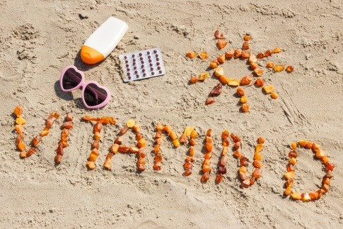 Sonnencreme und Sonnenbrille neben Schriftzug Vitamin D am Strand