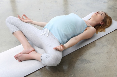 Eine schwangere Frau liegt am Rücken und meditiert