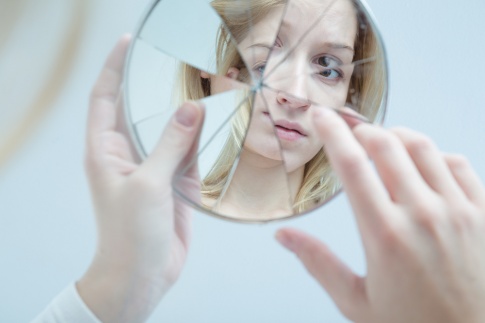 Eine Frau betrachtet sich in einem zerbrochenen Spiegel