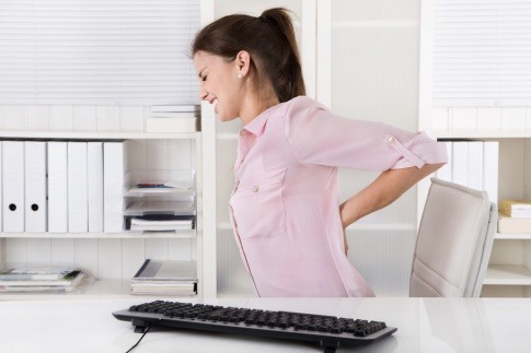 Eine Frau, die im Büro ist und von Rückenschmerzen geplagt wird