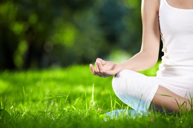 Eine Frau praktiziert Yoga. Es sind nur ihr Fuß und ihr Arm abgebildet, der Hintergrund ist grün. Die Yoga Position nennt sich Lotus-Pose.