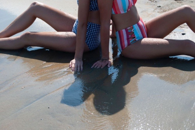 Zwei Frauen tragen eine hoch geschnittene Bikinihose und sitzen am Strand