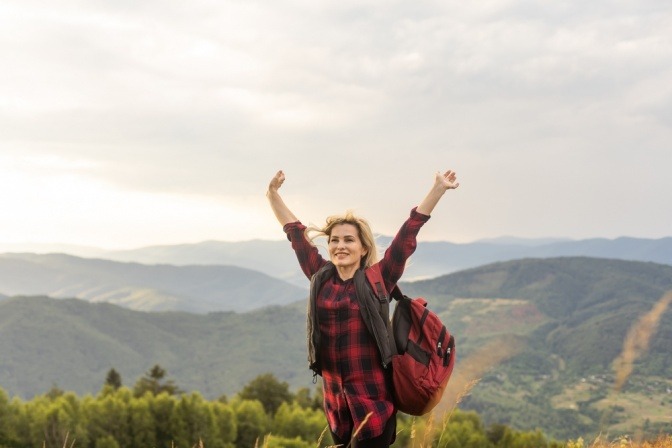 Frau auf dem Gipfel eines Berges genießt eine wunderbare Aussicht und wirkt glücklich und zufrieden.