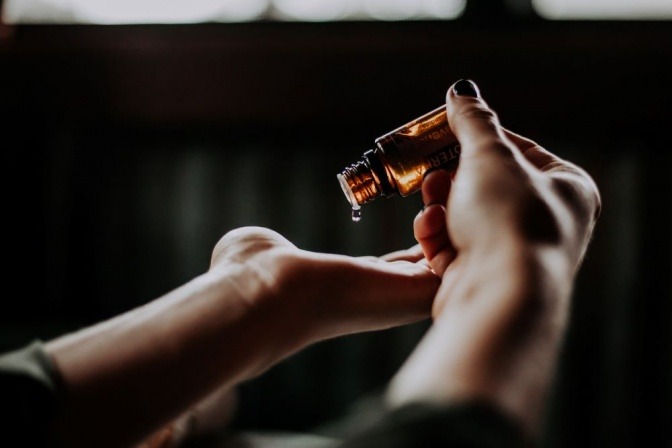 Öl-Tropfen fallen von einer braunen Flasche in die Handfläche einer Person