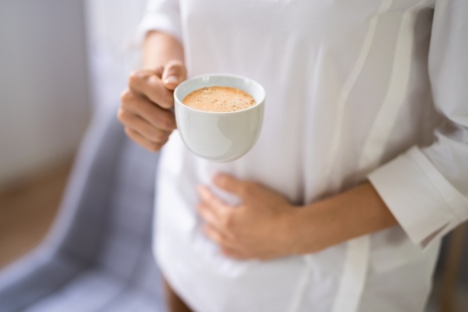 Mensch mit Kaffeetasse als abführendes Lebensmittel und Hand auf Bauch.