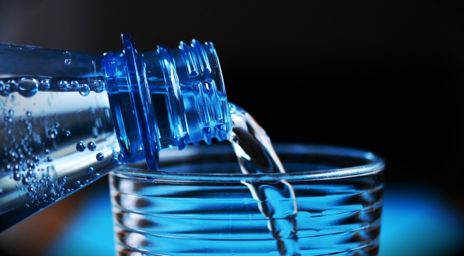 Wasser rinnt aus einer Flasche in ein Glas