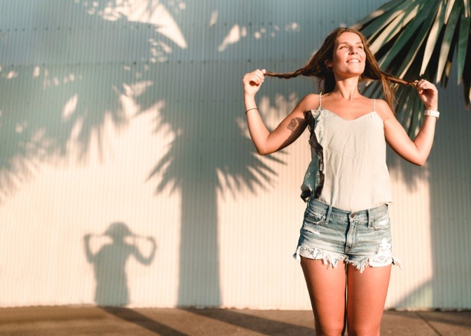 Eine fröhliche Frau reckt sich der Sonne entgegen, ihr Schatten ist in der Form eines jungen Mädchens mit Pferdeschwänzen.