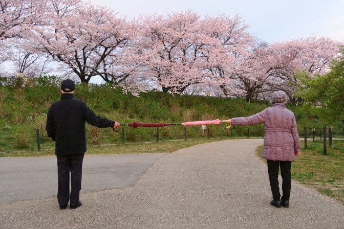 Zwei ältere Partner halten mit Schirmen Abstand