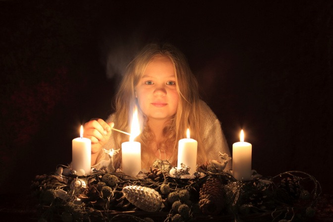 Mädchen zündet Kerzen am Adventkranz an