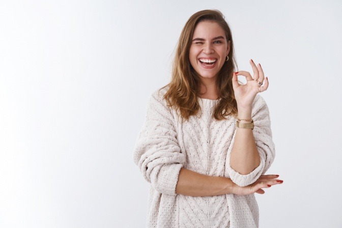 Eine lachende Frau macht mit ihrer Hand ein Ok Zeichen