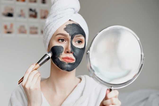 Frau trägt schwarze Gesichtsmaske mit Aktivkohle auf