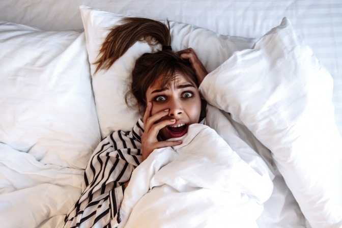Was hilft gegen Albträume? Verängstigte Frau nach einem Albtraum im Bett.