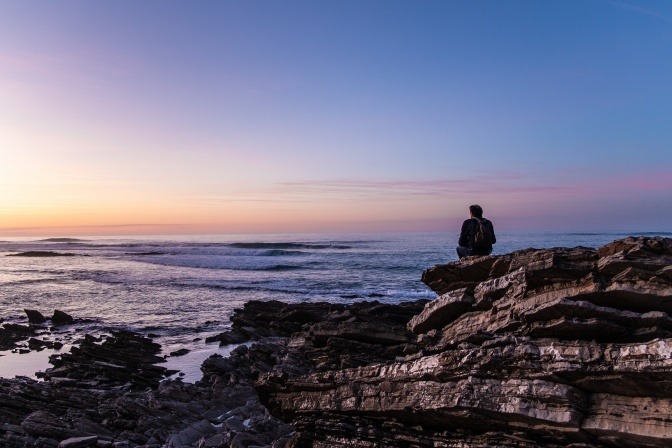 Ein Mann sitzt einsam und alleine auf Felsen am Meer