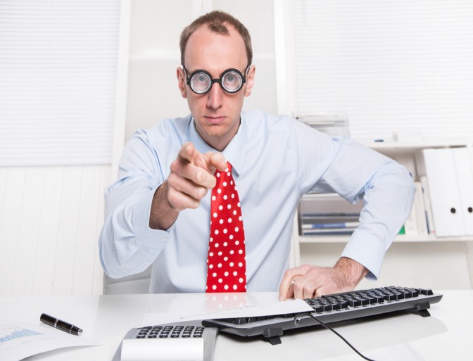 Ein Mann mit Brille und Krawatte sitzt im Büro und zeigt mit dem Finger nach vorne