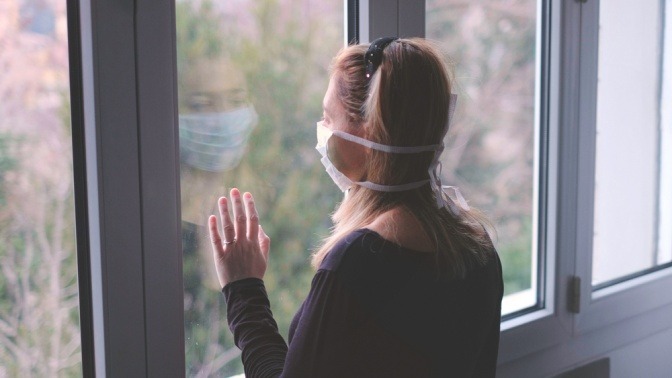 Eine Frau trägt einen weißen Mundschutz und schaut aus dem Fenster