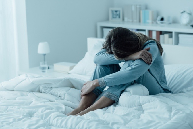 Frau sitzt depressiv am Bett