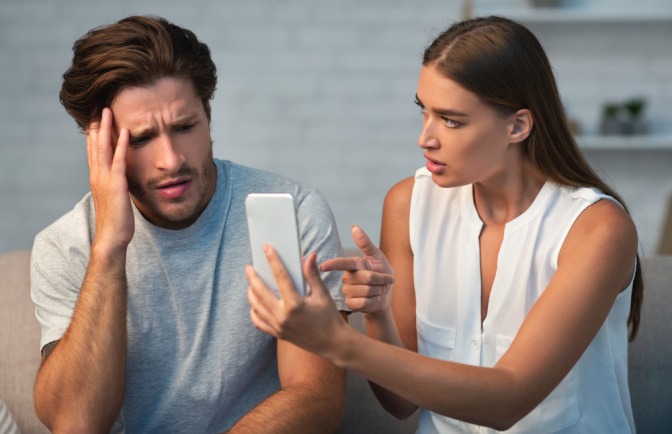 Frau zeigt eifersüchtig und wütend einem Mann ein Smartphone