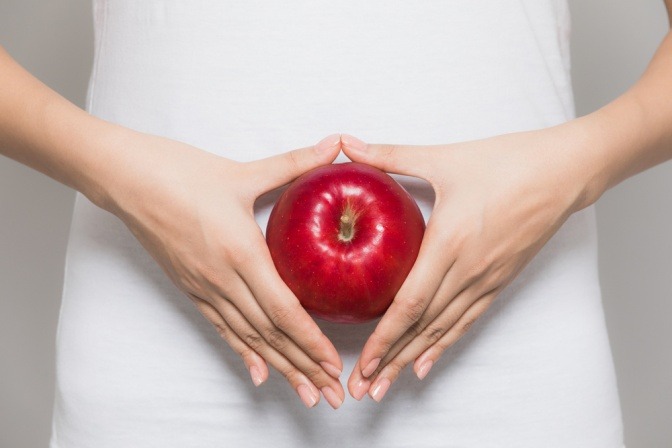 Frau hält Apfel vor ihren Bauch
