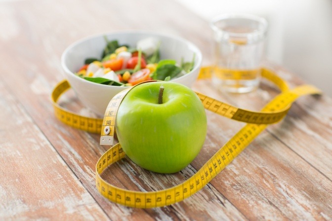 Ein Maßband liegt um einen Apfel und eine Schüssel mit Salat