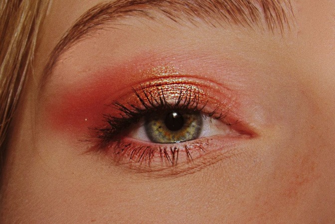 Ein grünes Auge mit glitzerndem schimmernden Augen-Make-up in Orangeton