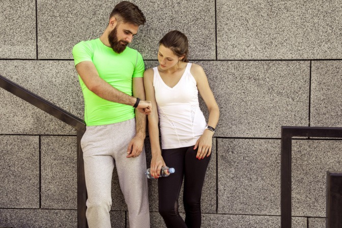 Ein Mann im Sportoutfit zeigt einer Frau seinen Schrittzähler am Arm