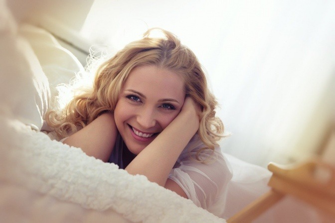 Eine Frau lächelt ausgeschlafen auf einem Bett