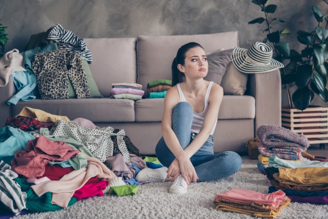 Eine frustrierte junge Frau sitzt auf dem Teppich in einem unordentlichen Wohnzimmer