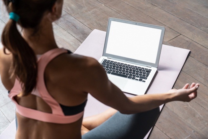 Sportliche junge Frau sitzt meditierend vor dem Laptop.